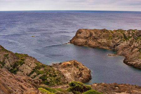 Rocky coast showing a natural bay and vast blue sea with a small boat navigating, creating a sense of remoteness and calmの写真素材