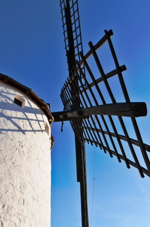 Traditional Spanish windmill with white wall and wooden blades creating shadows under a clear, bright blue sky in La Manchaの写真素材
