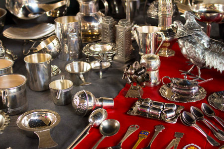 Silver cutlery (spoon, cups and other objects) displayed over a red carpet and gray table. The silver objects are polished and shiningの写真素材