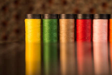 Row of yellow, green, brown, red, pink and orange threads with a reflection effectの写真素材