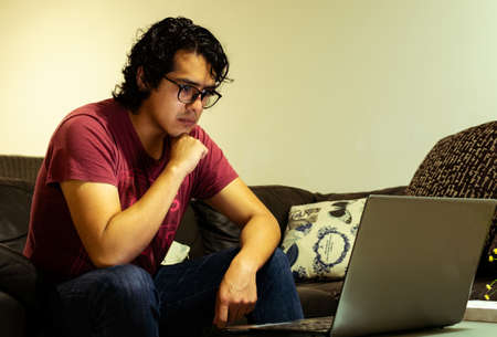 very worried guy looking a laptop sit in a couch wearing glassesの写真素材