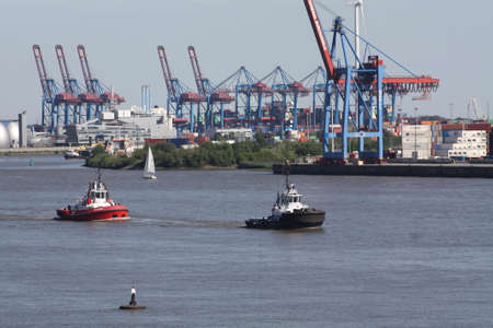 View of the Elbe with tugs and sailing boats. There are harbor cranes in the background.の写真素材