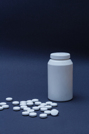 White pills medicine and plastic bottle behind on dark backgroundの写真素材