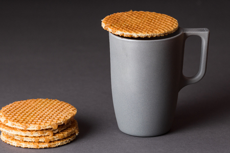 A glass cup of black tea with stack of dutch waffles on dark grey background.の写真素材