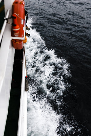 Sea splashes near a sea vessel. White yacht or ship with red lifeline, dark deep water of ocean or...