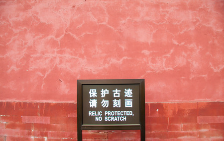 Sign with a typical Chinglish phrase "Relic protected, no scratch" in front of an ancient red wall in the Forbidden City in Beijing, Chinaのeditorial素材