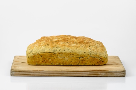 Side view of a Loaf of Herb and Garlic Soda Bread presented on a Bread Board Isolated on White