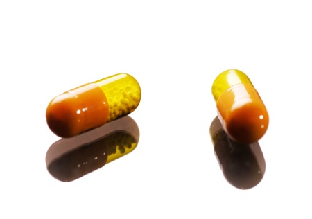 Two yellow and orange color capsule pills against white backgroundの写真素材