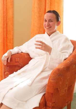 Young woman in bathrobe holding glass of waterの写真素材