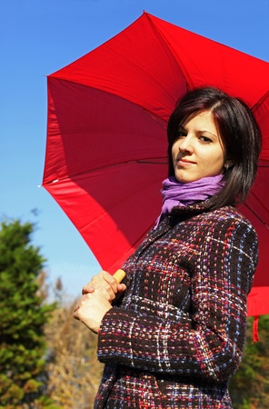 Young woman standing outdoor with red umbrellaの写真素材
