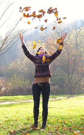 Woman throwing yellow leaves in the air in autumnの写真素材