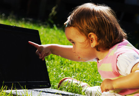 Adorable little girl playing with laptop on green grassの写真素材