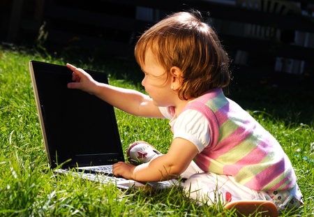 Adorable little girl playing with laptop on green grassの写真素材