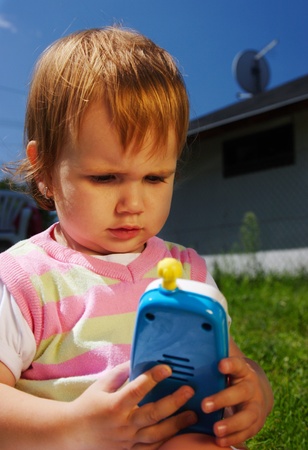 Young girl child outdoor sitting on the grass with her toy phoneの写真素材