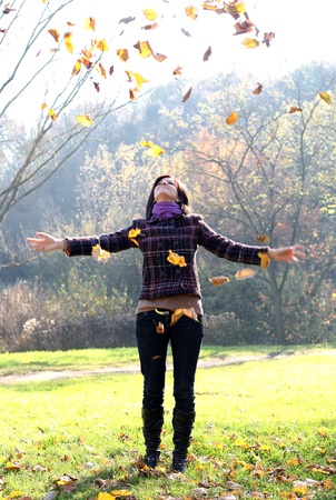 Woman throwing yellow leaves in the air in autumnの写真素材