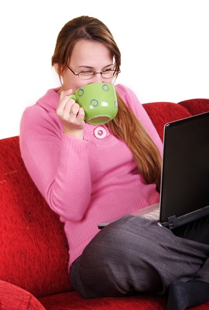 Young woman sitting on red couch with laptop and mugの写真素材