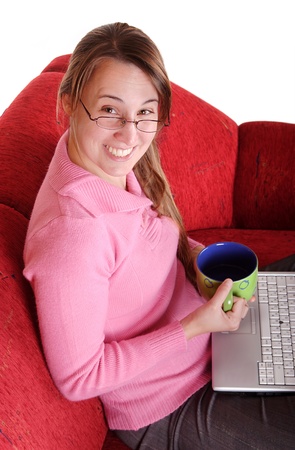 Young woman sitting on red couch with laptop and mugの写真素材