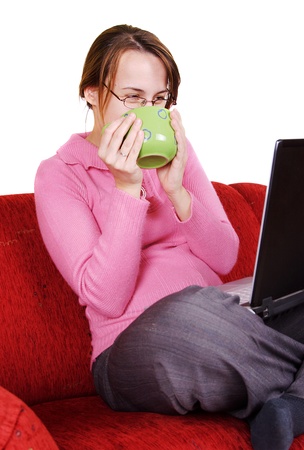 Young woman sitting on red couch with laptop and mugの写真素材