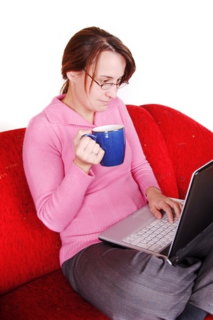Young woman sitting on red couch with laptop and mugの写真素材