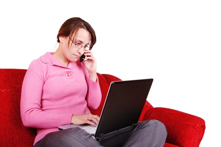 Young woman sitting on red couch with laptop and mug and phoningの写真素材