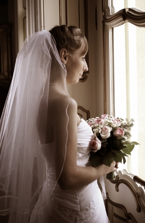 Beautiful bride in white wedding dress standing near the windowの写真素材