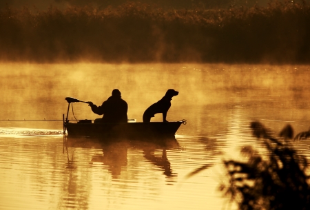 Silhouette of fisher and dog sitting in boatの写真素材
