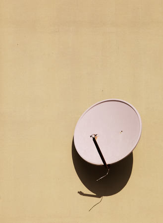 Television satellite dish against a yellow wallの写真素材