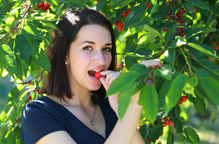 Young girl eats cherry outdoor from cherry tree
