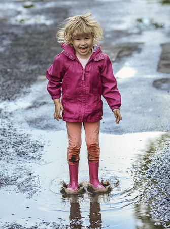 Playful child outdoor jump in puddle in boot after rain