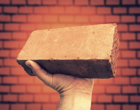 Hand hold red brick against brick wallの写真素材