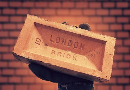 Hand hold red brick against brick wallの写真素材