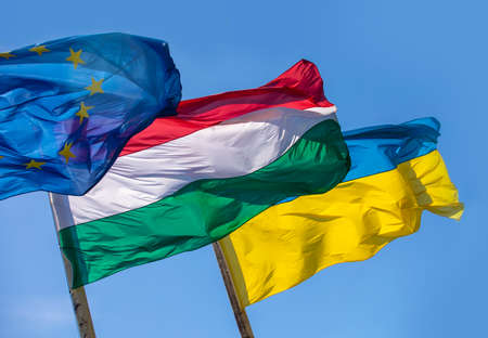 Flags of Hungary Ukraine and European Union waving on pole against blue skyの写真素材