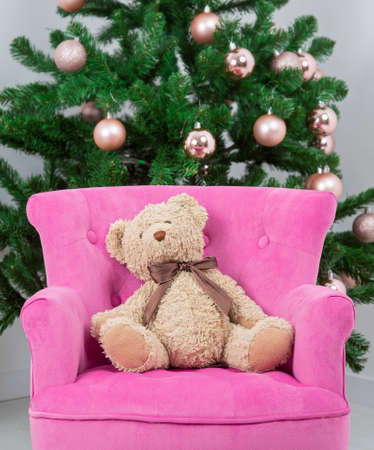 Teddy bear sitting in pink armchair in background christmas treeの写真素材