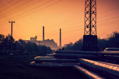 Industrial landscape with pipes of thermal power plant against orange sunset skyの写真素材