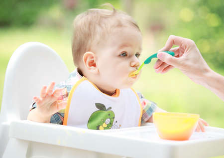 Mother feeding her baby boy with spoon in the garden. Healthy food.の写真素材