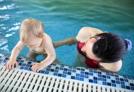 Cute baby girl learning to swim in swimming pool with her motherの写真素材