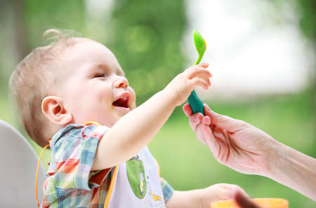 Cute little baby boy with green leaves in his mouth playing outdoors.の写真素材