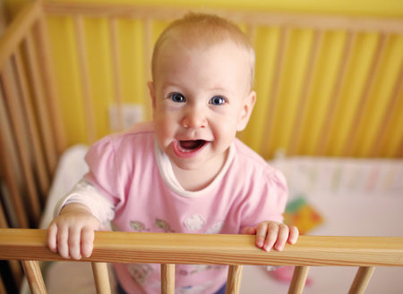 Cute baby girl standing in crib at home. Happy childhood conceptの写真素材
