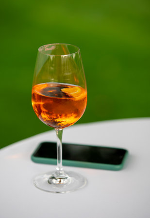 Glass of prosecco with mobile phone on table outdoorの写真素材