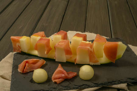 juicy melon with ham typical summer food on dark backgroundの写真素材