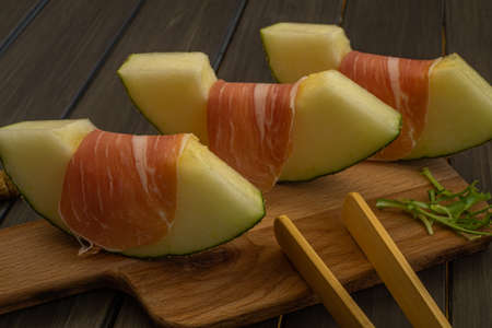 juicy melon with ham typical summer food on dark backgroundの写真素材