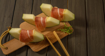 juicy melon with ham typical summer food on dark backgroundの写真素材