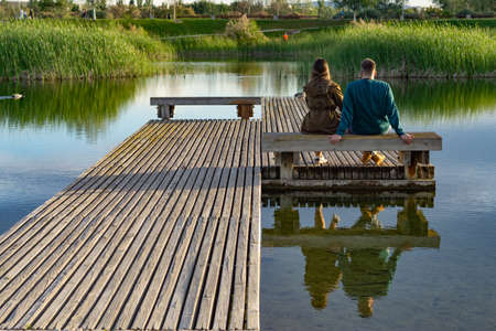 young couple sitting on the shore of a lake looking at the waterの写真素材