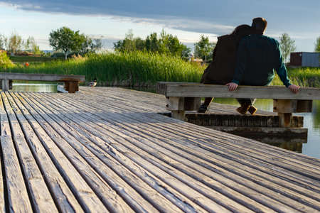 young couple sitting on the shore of a lake looking at the waterの写真素材