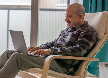 man watching pc and paying online, drinking coffee in the living room of his homeの写真素材