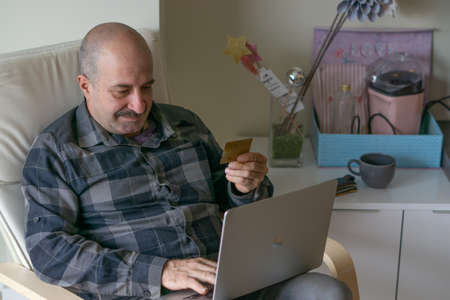 man watching pc and paying online, drinking coffee in the living room of his homeの写真素材