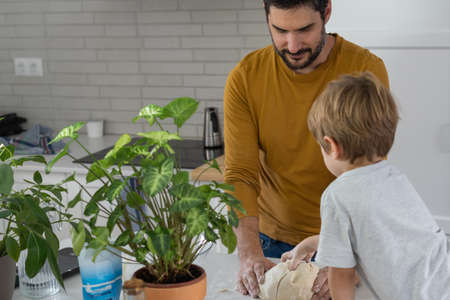 young man making homemade bread with his son in his home kitchenの写真素材