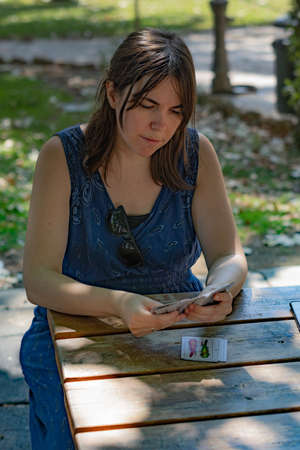 young woman playing cards in the park on a sunny day wearing a blue dress
