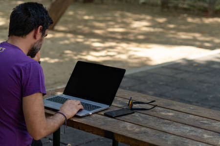 young man working at his computer on a wooden table in the park on a sunny dayの写真素材