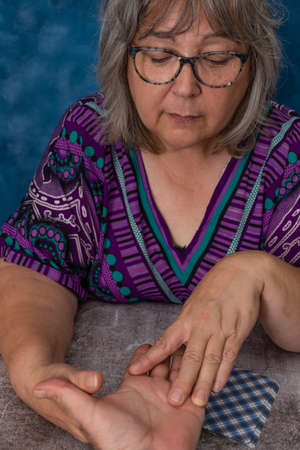 older white-haired woman reading tarot cards on a wooden table with candleの写真素材
